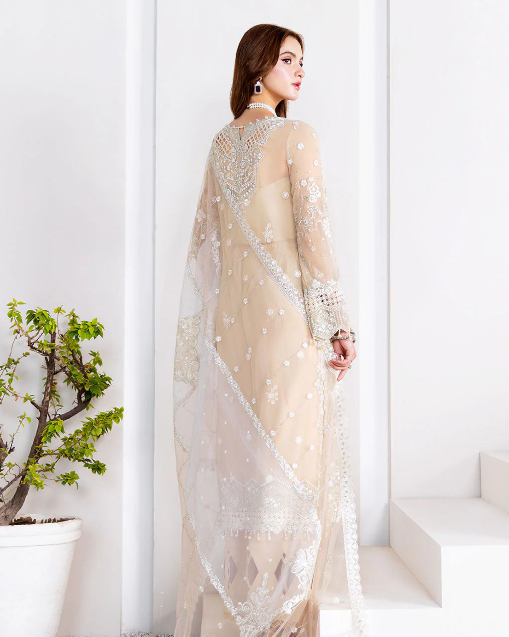 Woman wearing a beige saree with white embroidery in a minimalistic setting.