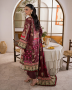 Woman in a burgundy embroidered outfit standing in a room with a table and chairs.