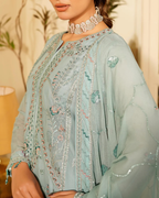 Light blue embroidered traditional outfit with a necklace against a blurred indoor background