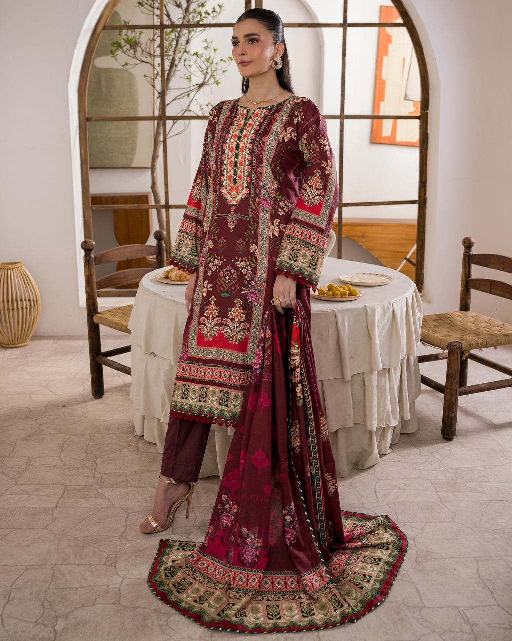Woman in a traditional embroidered outfit standing in a room with a table and chairs.
