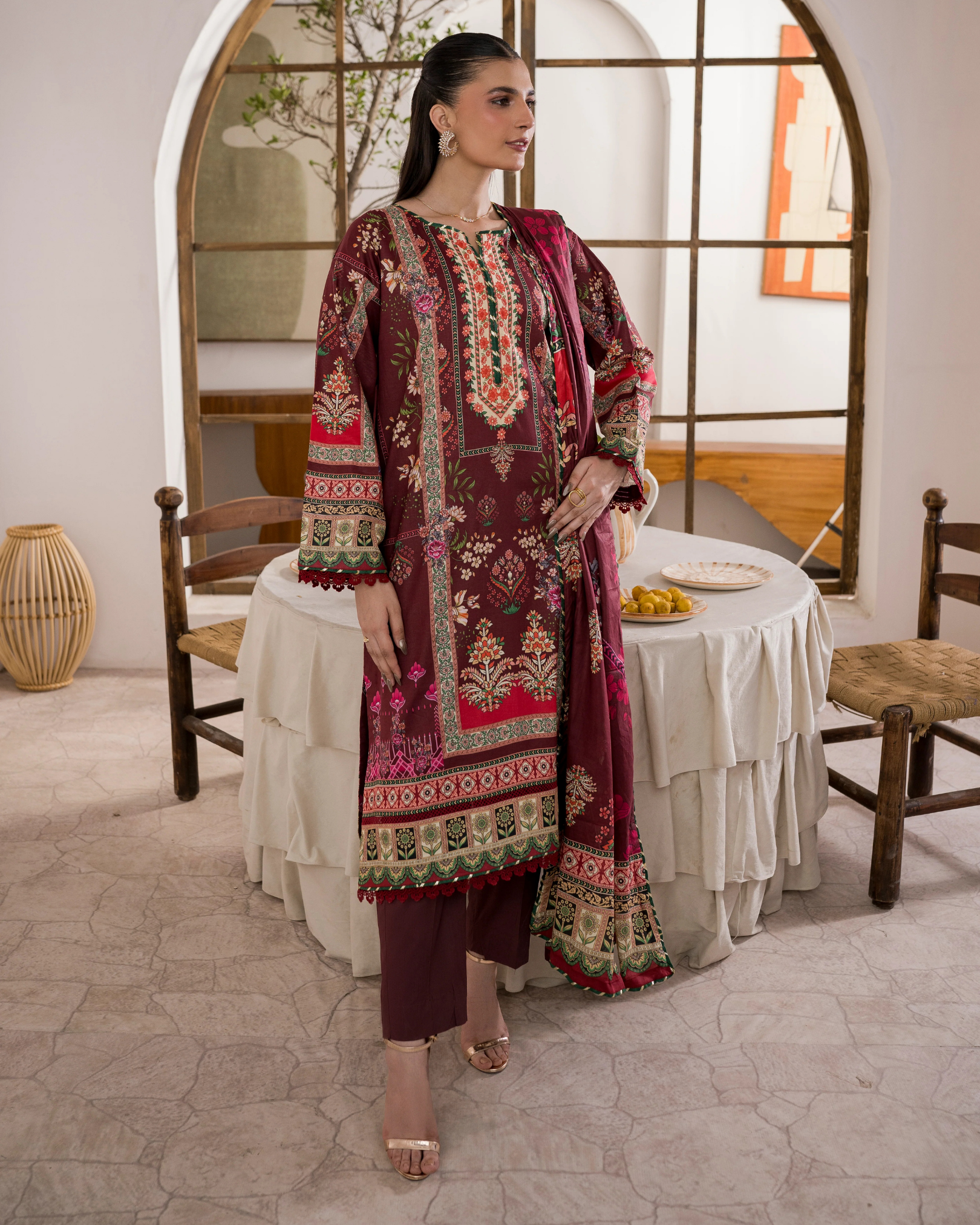 Woman in an embroidered traditional outfit standing in a room with a table and chairs.