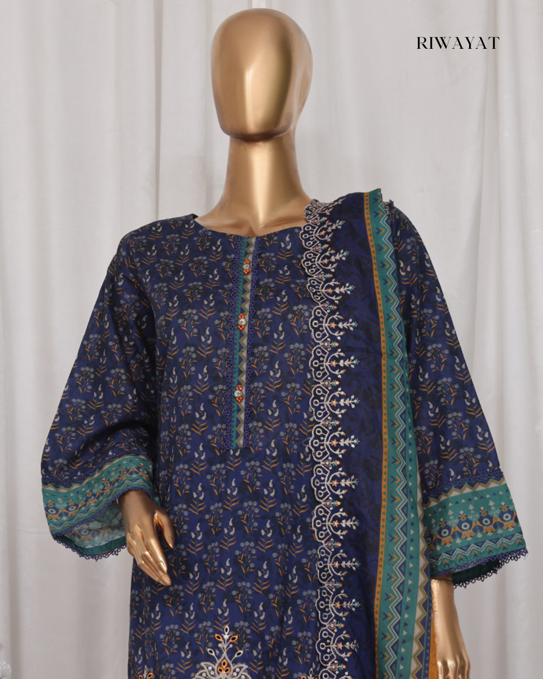 Mannequin wearing a blue embroidered dress with green and gold details against a white background, branded 'RIWAYAT'.