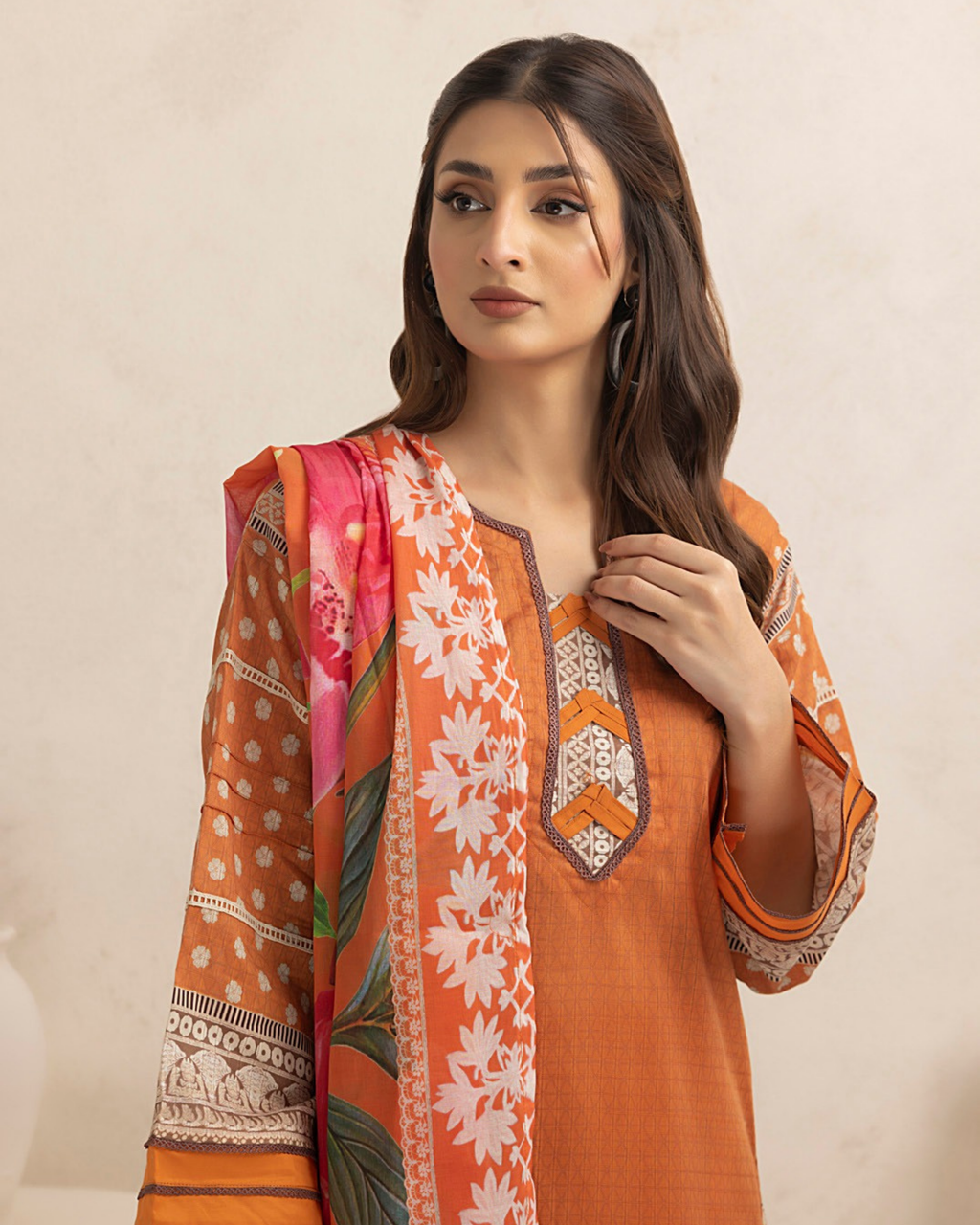 Woman wearing an orange floral dress with a matching dupatta on a beige background