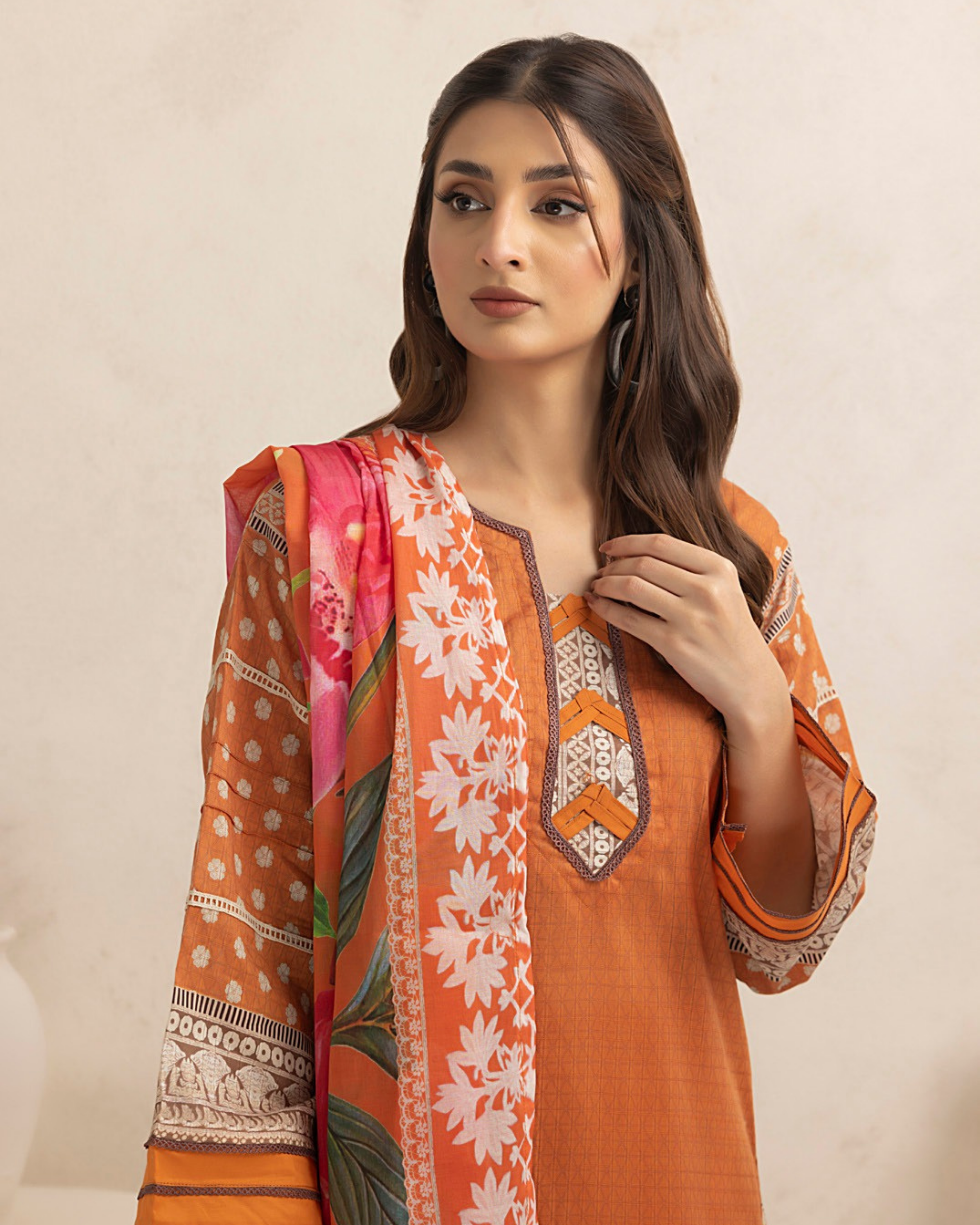 Woman wearing an orange floral dress with a matching dupatta on a beige background