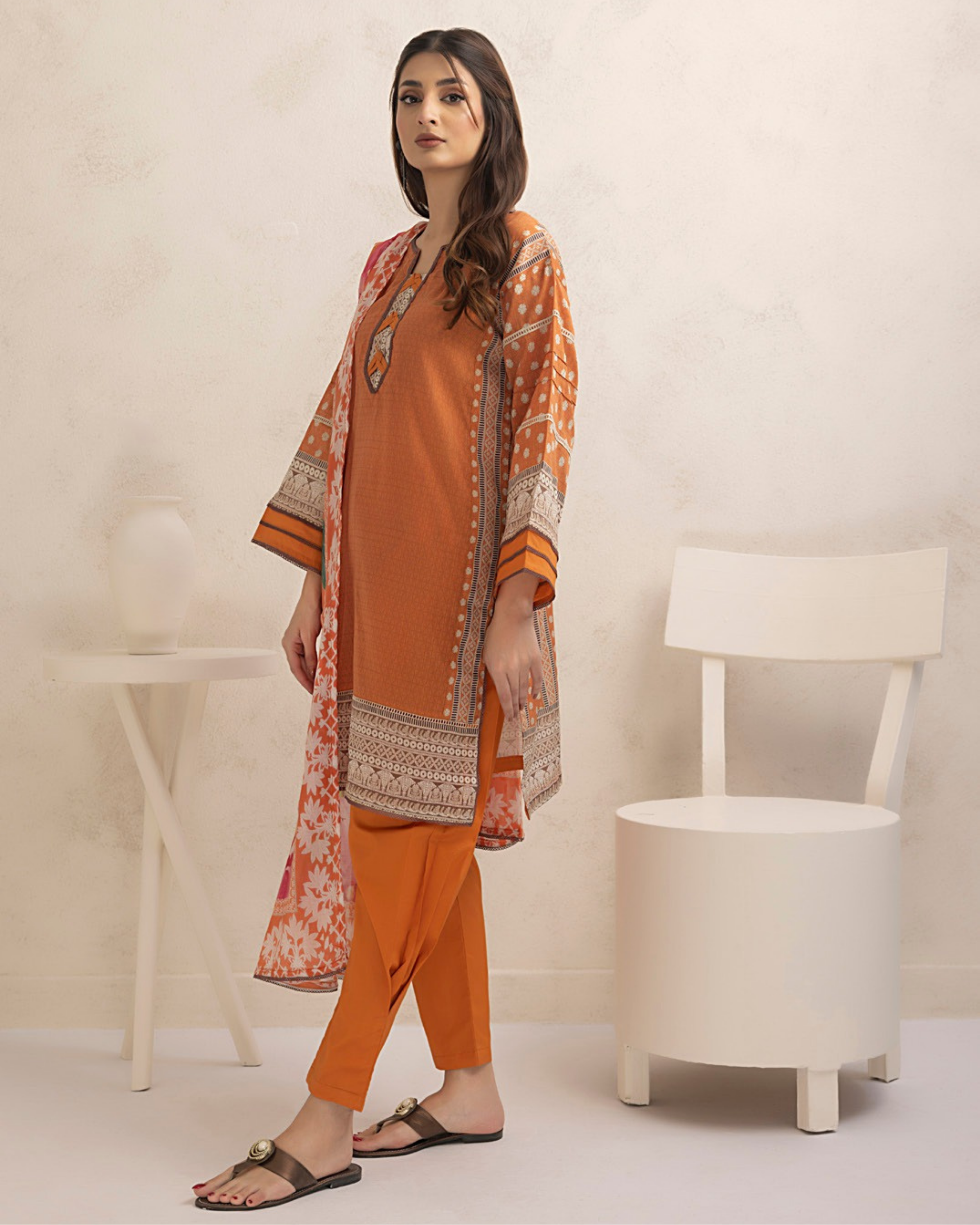 Woman wearing an orange and patterned outfit with a white chair in the background