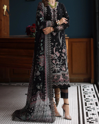 Woman wearing a long, dark embroidered dress in an indoor setting with wooden paneling.