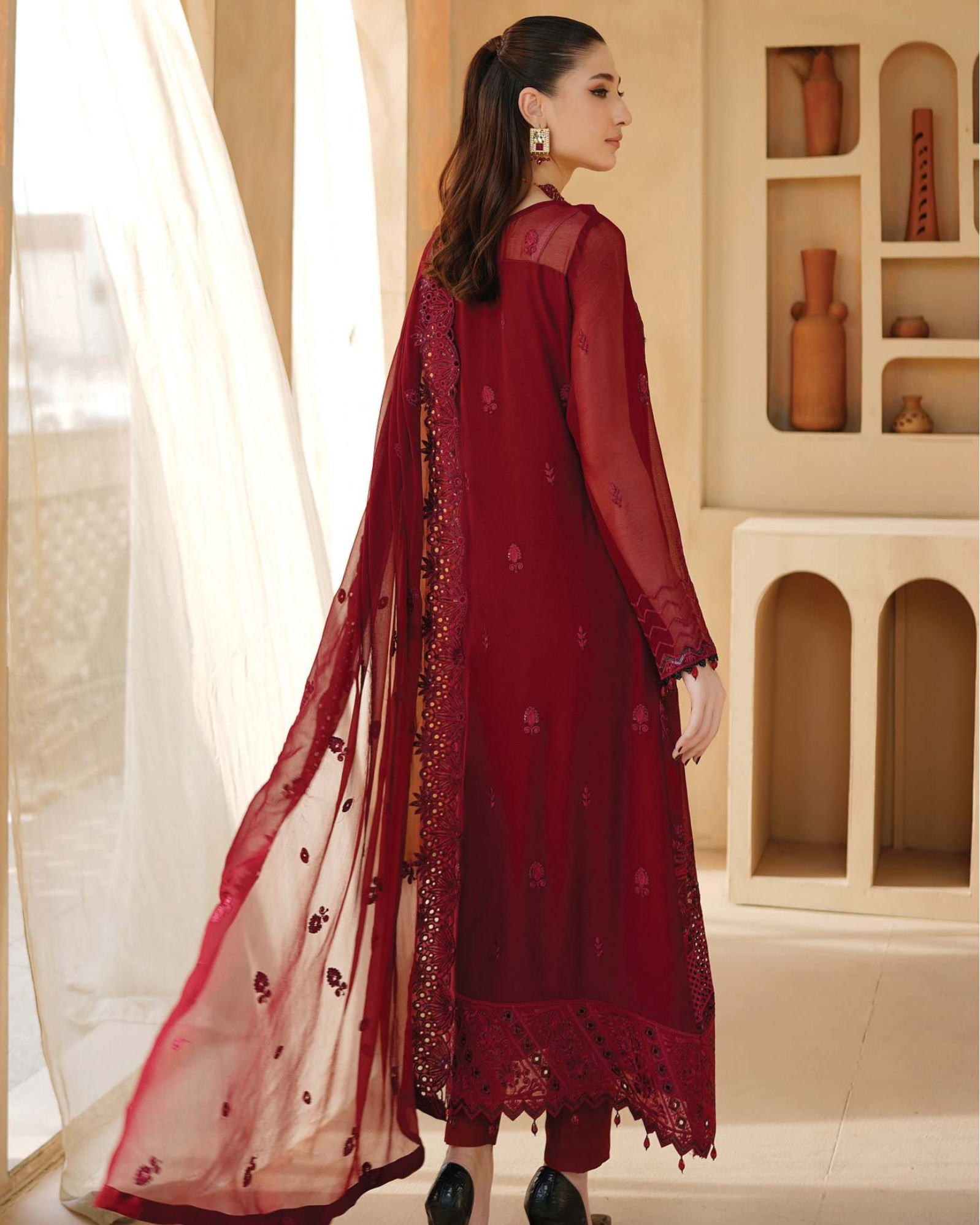 Woman in a red traditional outfit with a sheer dupatta in a decorated room.