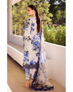 Woman wearing a blue and white floral outfit standing outdoors with greenery in the background