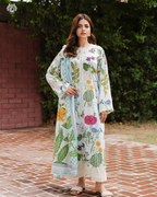 Woman wearing a floral dress standing outdoors on a brick path with greenery in the background