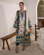Woman wearing a patterned dress in an indoor setting with wooden furniture and a white wall.