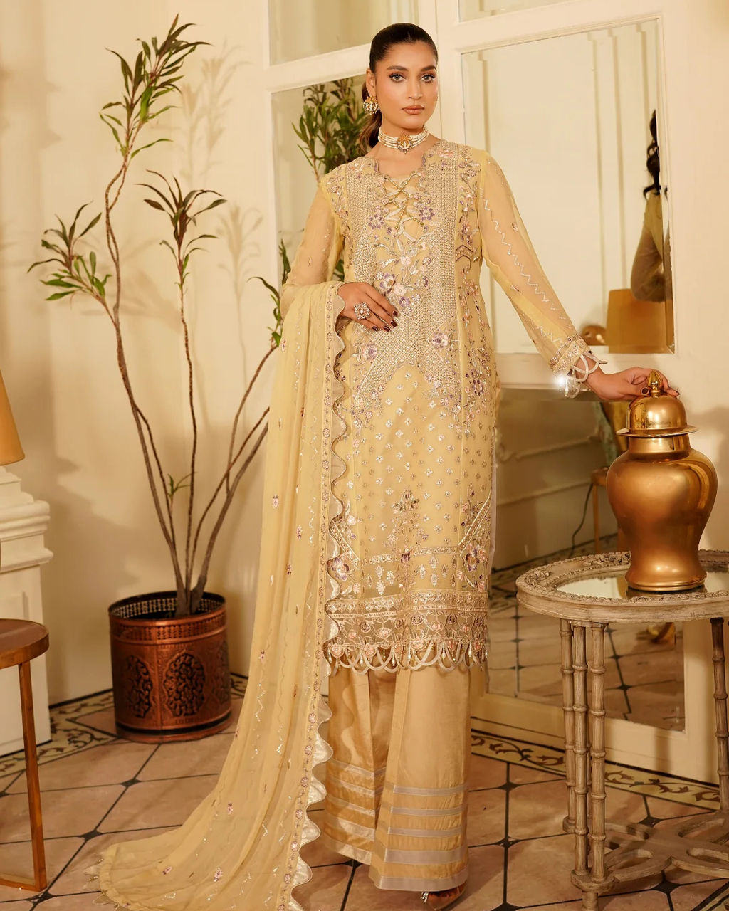 Woman in a beige embroidered traditional outfit standing in an elegant room.