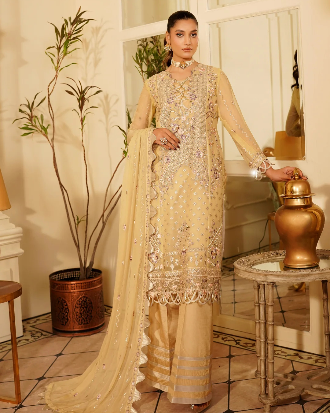 Woman in a beige embroidered traditional outfit standing in an elegant room.