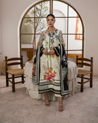 Woman in a floral dress with a matching shawl standing in a room with wooden chairs and a large mirror.