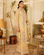 Woman in a beige embroidered traditional outfit standing in a decorated room.
