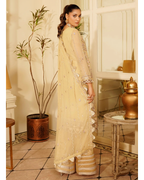 Woman in a beige embroidered saree standing in an elegant room with decorative elements.