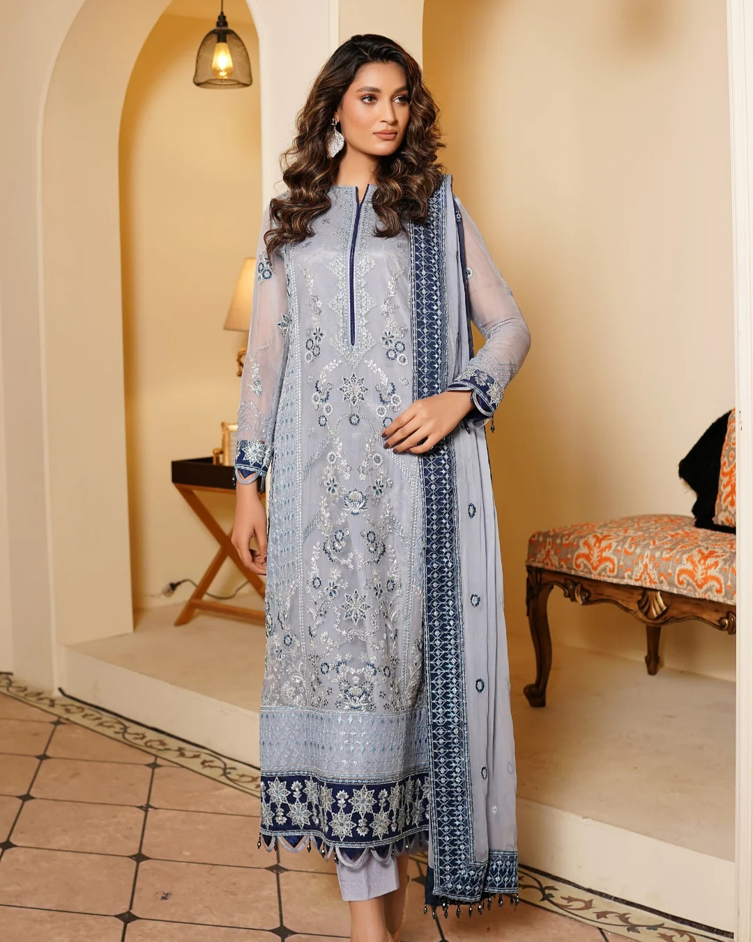 Woman wearing a light blue embroidered outfit with a matching dupatta in an indoor setting.
