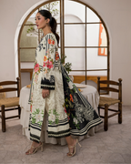 Woman in a floral embroidered outfit standing in a room with wooden chairs and a table.