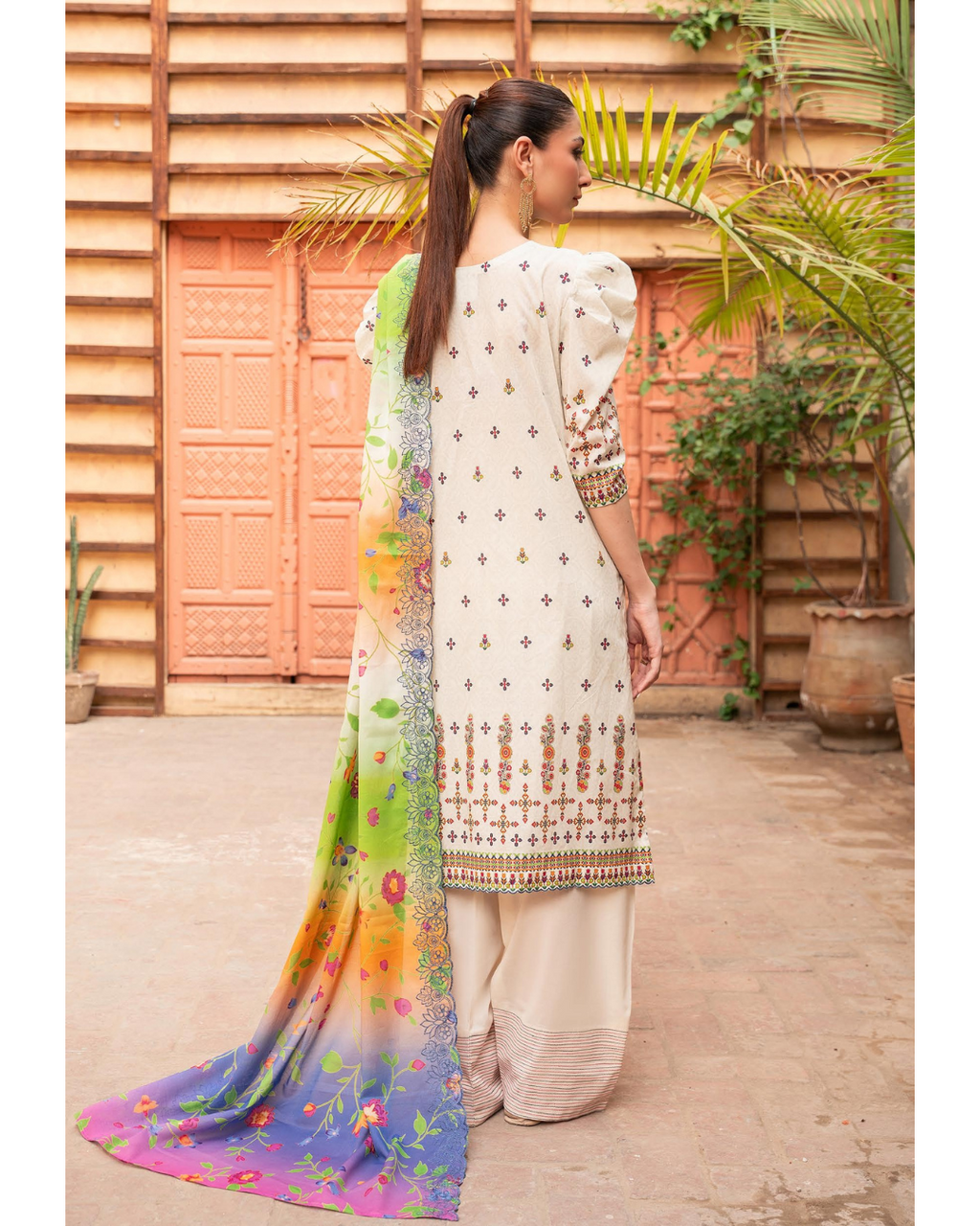 Woman in traditional outfit with colorful dupatta against a wooden door and plants background