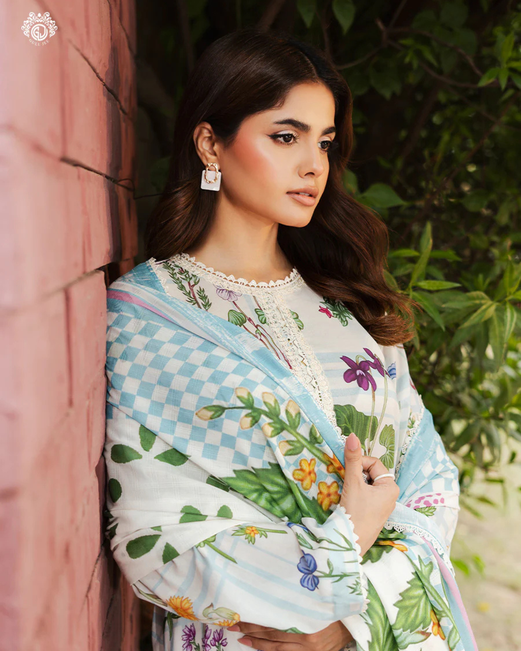 Woman wearing a floral saree with a checkered border, standing against a natural background.