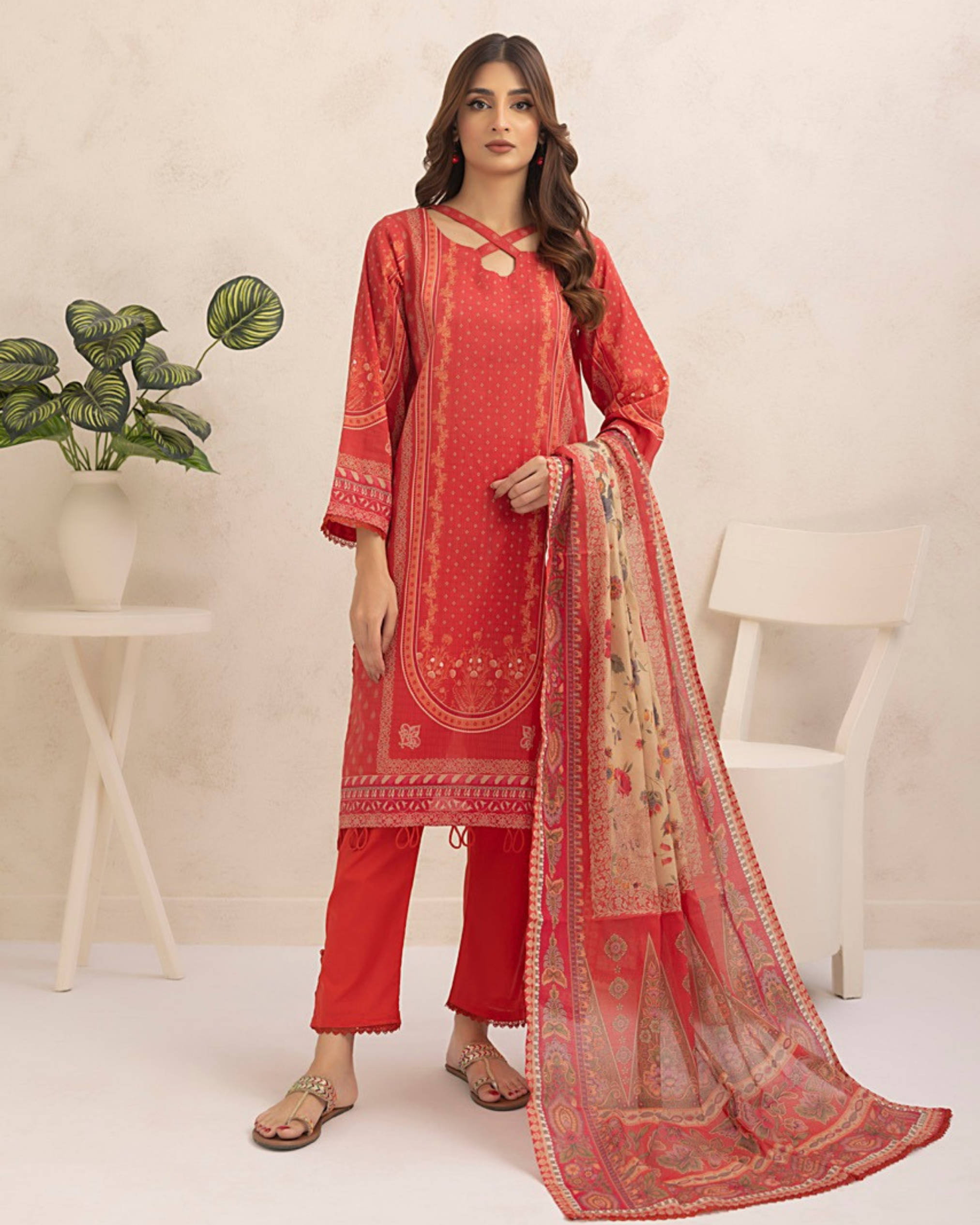 Woman wearing a red traditional outfit with a matching dupatta in a minimalistic setting.