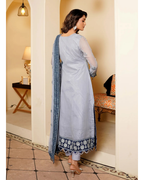 Woman in a light blue traditional outfit with white embroidery in a decorated room.