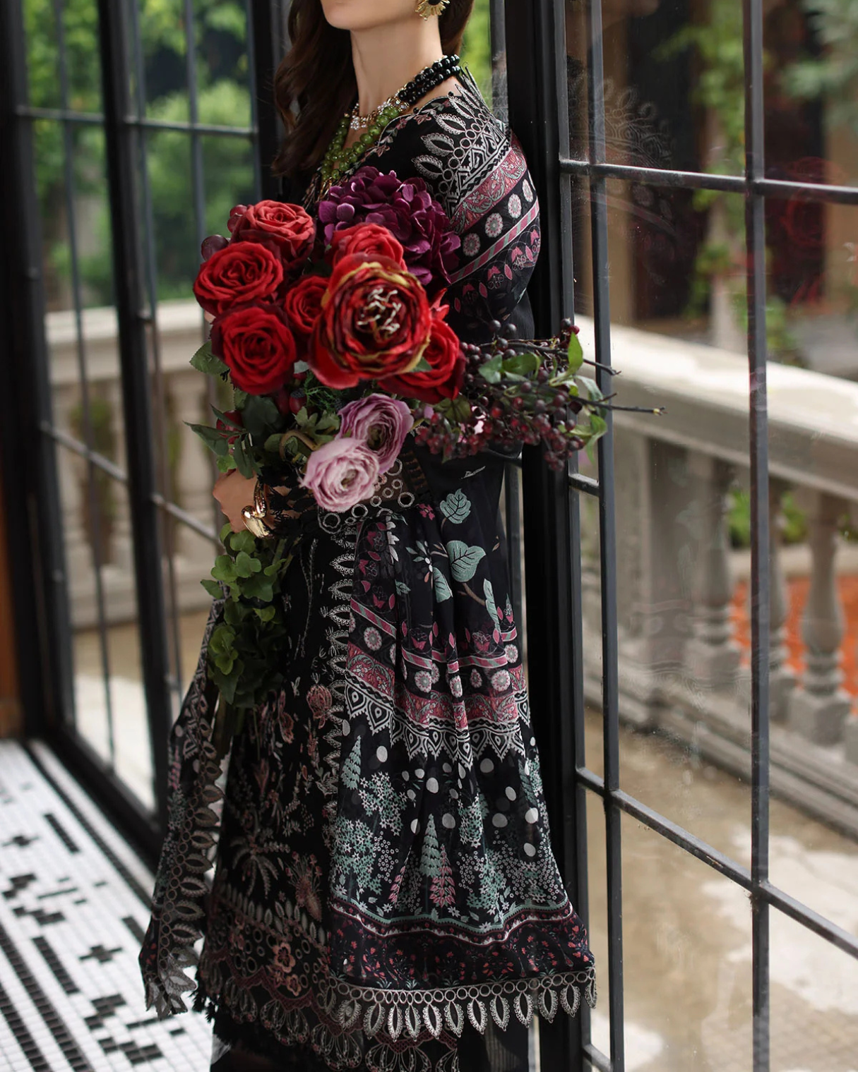 Mannequin wearing a patterned dress with a bouquet of flowers in front of a glass door.