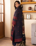 Woman wearing a dark blue traditional outfit with red patterns in a room.