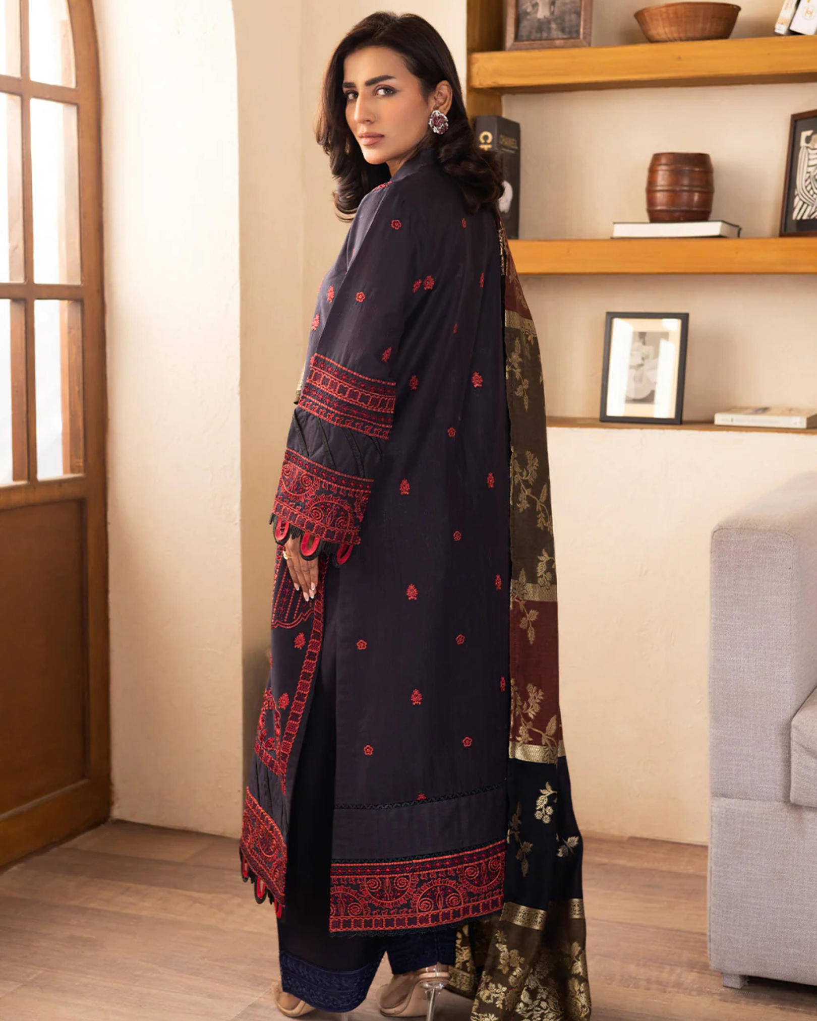 Woman wearing a dark blue traditional outfit with red patterns in a room.