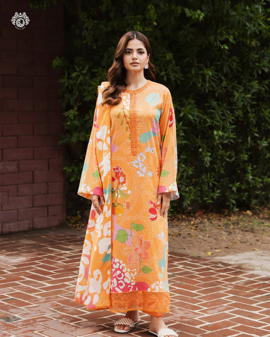Woman wearing an orange floral dress standing on a brick path with greenery in the background