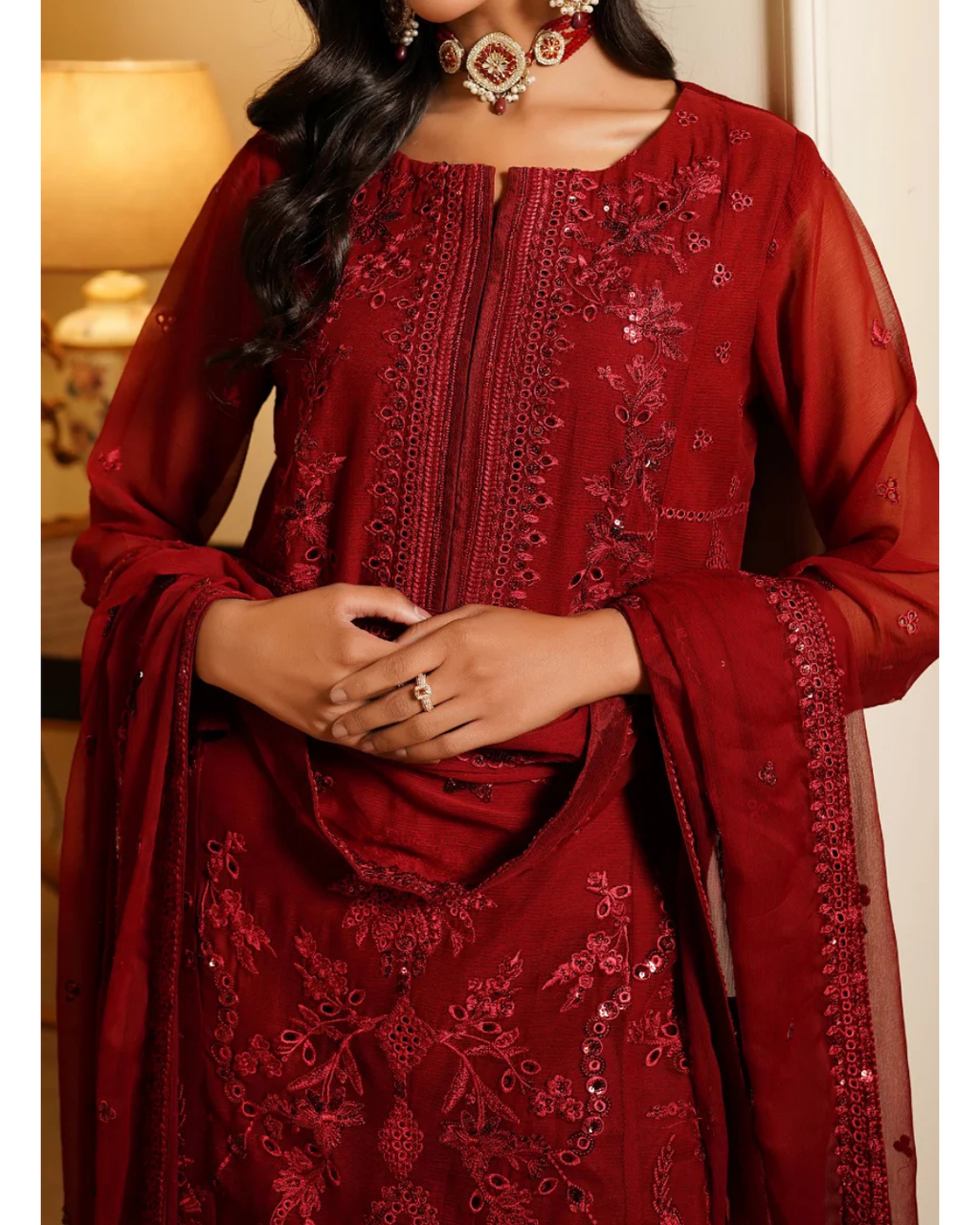 Red embroidered traditional outfit with matching dupatta, worn by a person indoors.