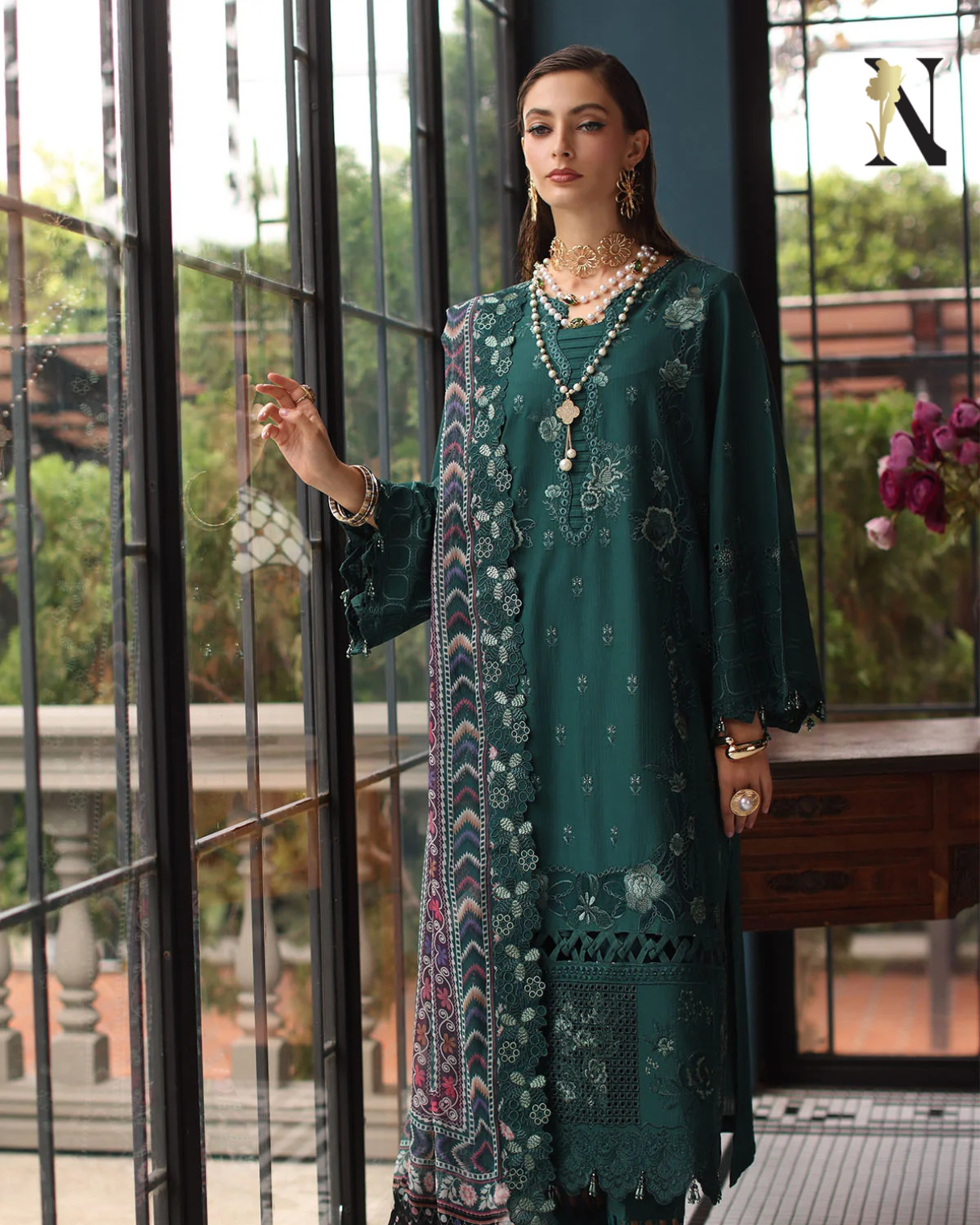 Woman in a green embroidered dress with a patterned shawl standing indoors.