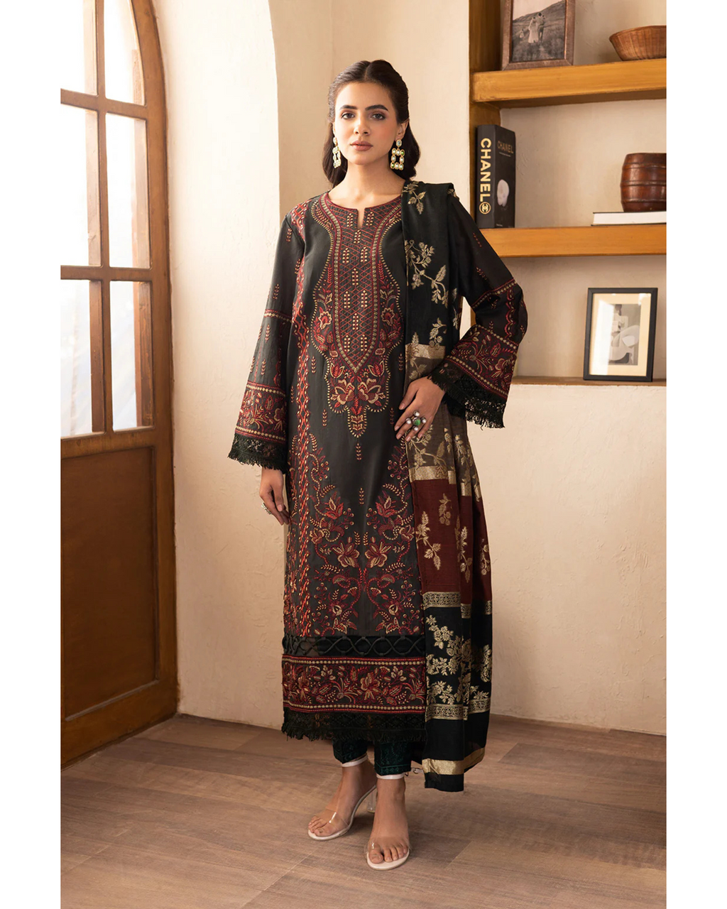 Woman wearing a traditional outfit with intricate patterns in a room with wooden shelves.