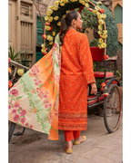 Woman in an orange traditional outfit with a floral dupatta standing next to a decorated entrance.