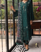 Woman wearing a green embroidered outfit with a patterned scarf indoors.
