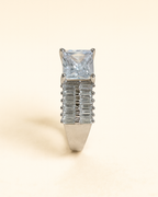 Silver ring with a large central gemstone and smaller baguette-cut stones on a beige background