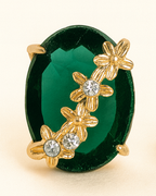 Pair of green earrings with gold floral designs and clear stones on a beige background