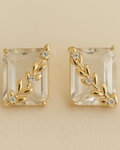 Gold earrings with clear gemstones on a beige background