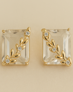Gold earrings with clear gemstones on a beige background