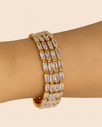 Gold bracelet with clear stones on a wrist against a beige background