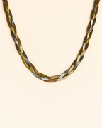 Braided necklace with gold, silver, and bronze tones on a beige background