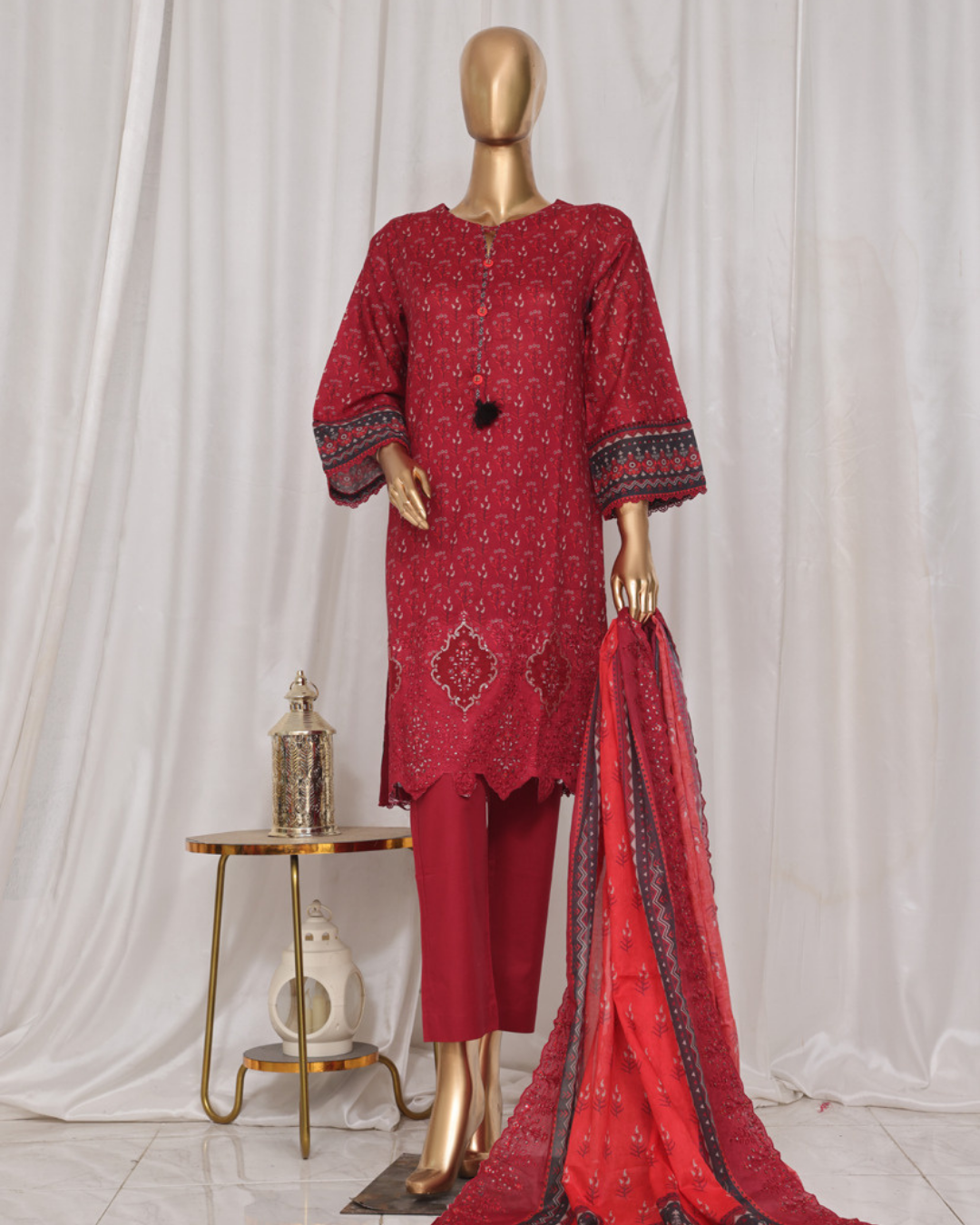 Red patterned outfit with matching dupatta on a mannequin against a white curtain background