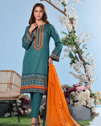 Woman in teal embroidered dress with orange dupatta standing outdoors with flowers and chair in background