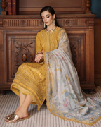 Woman in traditional yellow and white embroidered outfit sitting on a wooden bench.