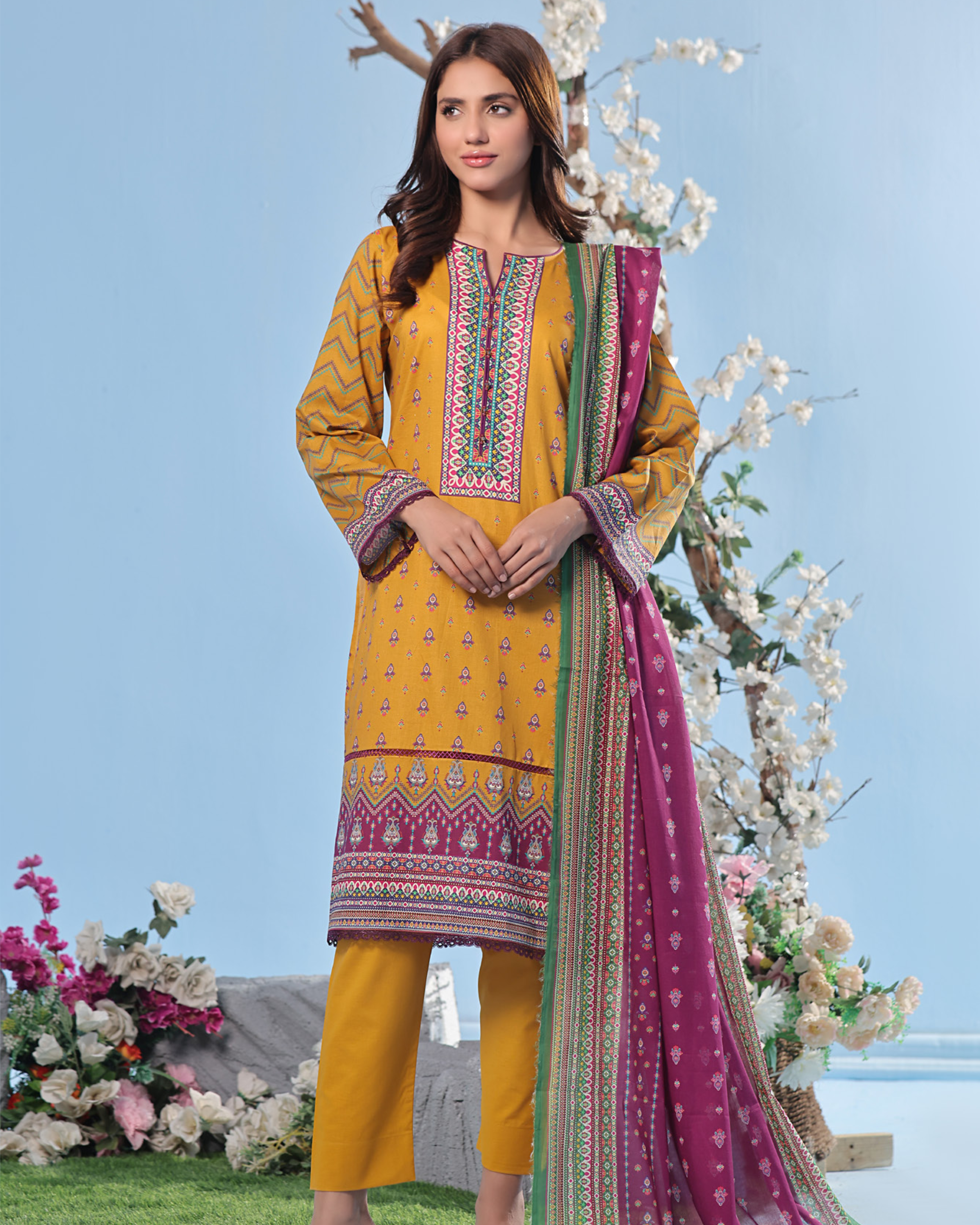 Woman wearing a yellow and pink traditional outfit with floral decorations in the background